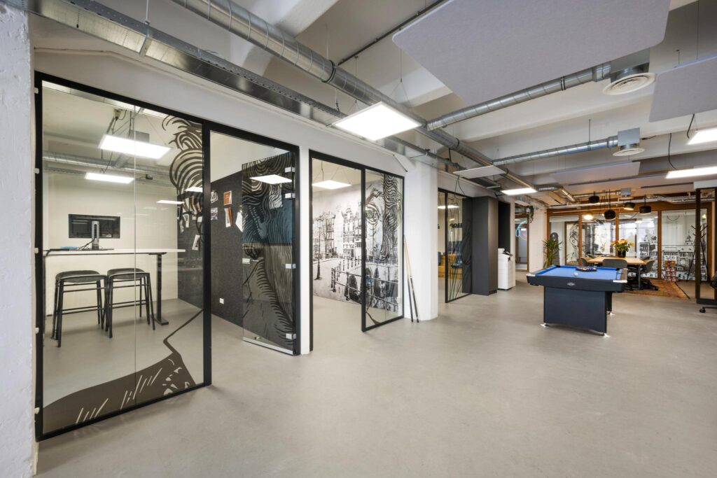 Modern office interior on Van Diemenstraat with glass meeting rooms, a pool table, and graphic wall art.